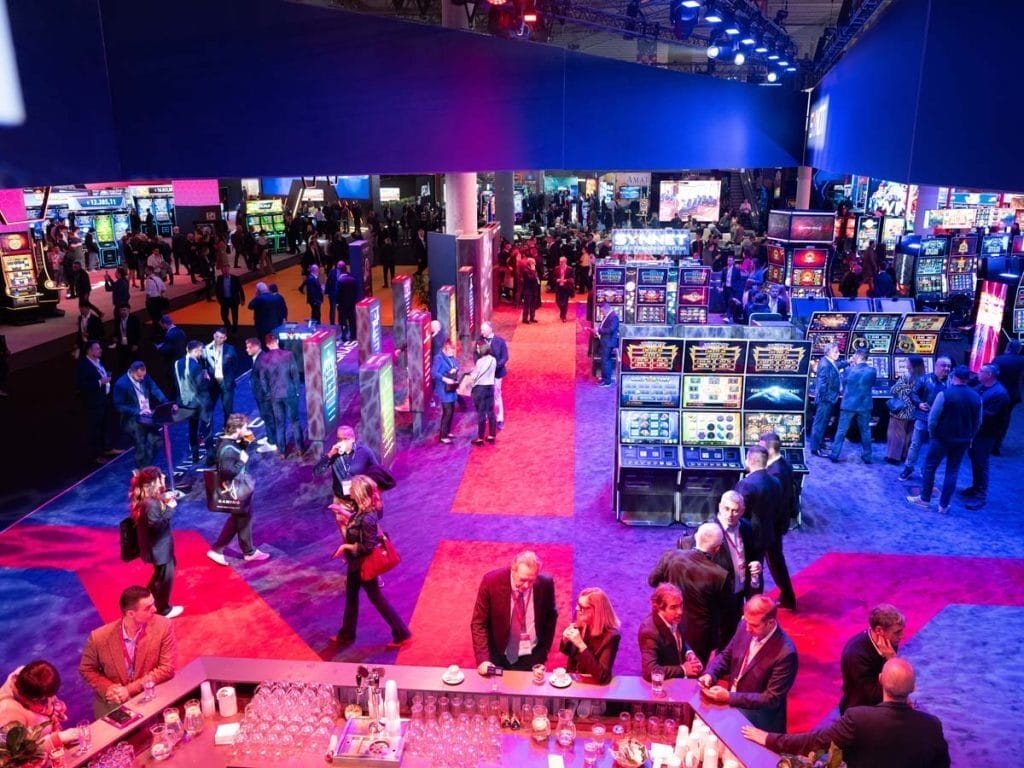 Ilustración digital estilo concept art que muestra un stand de feria de videojuegos concurrido en Barcelona, con pantallas mostrando el juego Neva y desarrolladores hablando con jugadores, iluminación cálida y atmósfera de celebración.